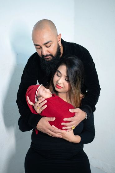 A loving couple tenderly holds their newborn baby wrapped in red.