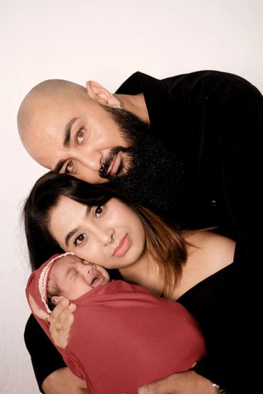 A loving family portrait with a father, mother, and crying baby wrapped in a red blanket.