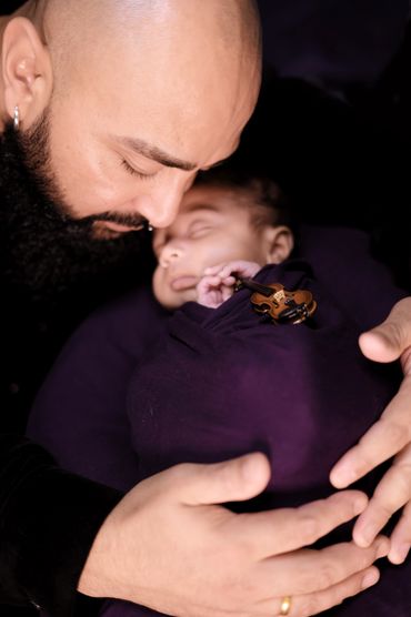 A tender moment between a father and his sleeping baby wrapped in a purple blanket with a miniature violin.