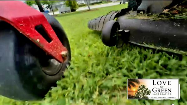 Close-up of a lawn mower cutting grass with a landscaping logo.