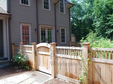 Wooden fence with gate enclosing a backyard garden next to a house.