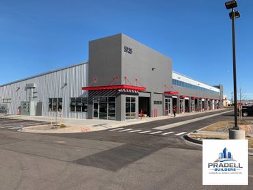 Modern commercial building with gray walls and red accents under clear blue sky.
