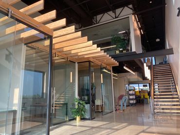 Modern office with glass walls, wooden beams, and a staircase.