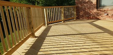 Pressure treated deck with handrails facing brick house.