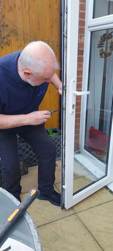 A man fixing a white door lock with a screwdriver outdoors.
