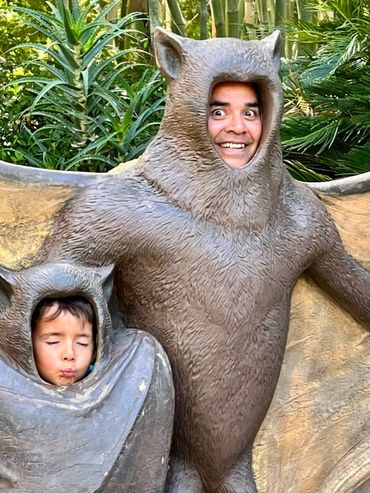 Two people posing with faces in bat statues, one smiling and one puckering lips.