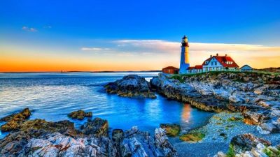 Lighthouse on rocky coast during sunset.