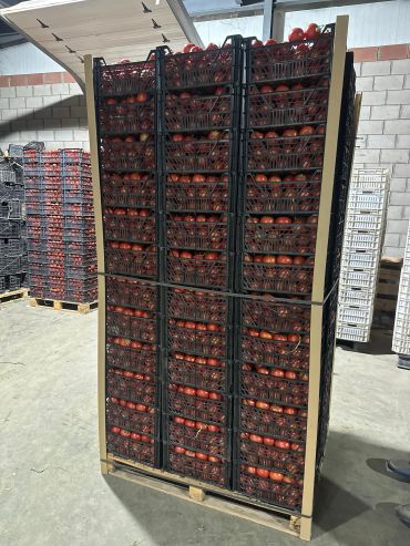 Stacked crates of red tomatoes on a pallet in a warehouse.