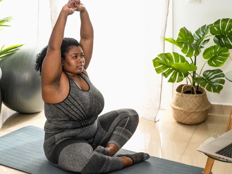 Woman in workout clothes stretching on a yoga mat indoors.