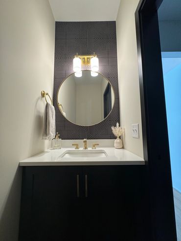 Modern bathroom vanity with black geometric wallpaper and gold fixtures.