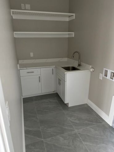 West Michigan modern laundry room with white cabinets, utility sink, and open shelving for added storage and functionality.