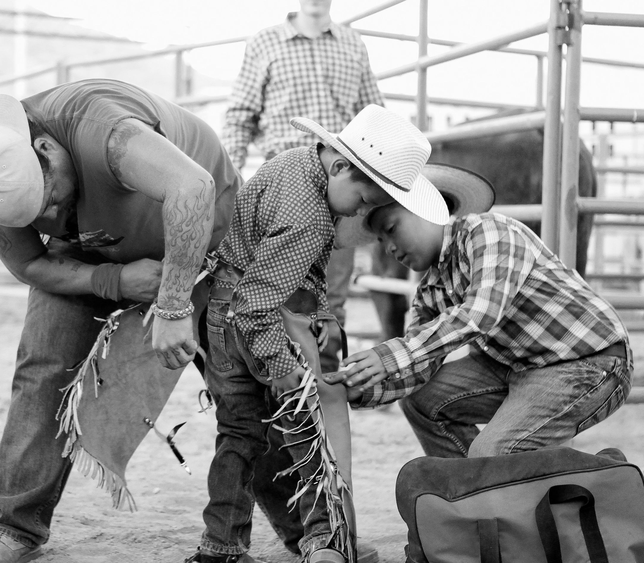 Two adults help a young man secure his chaps at the Springville Rodeo in Springville, California.