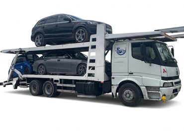 A white car transporter truck carrying two dark-colored cars.