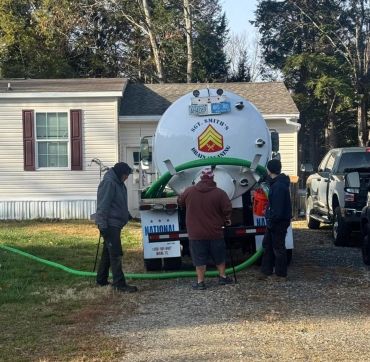 Three men working with a septic tank service truck in a residential area.