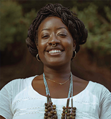 Smiling woman with braided hair and beaded necklace outdoors.