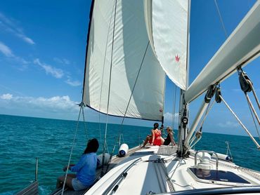 Girls are enjoying a sailboat charter in the clear blue waters of Marathon, FL, under a sunny sky.