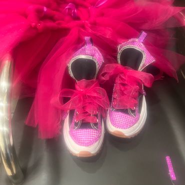 Pink sparkly sneakers with ribbon laces next to a bright pink tutu.