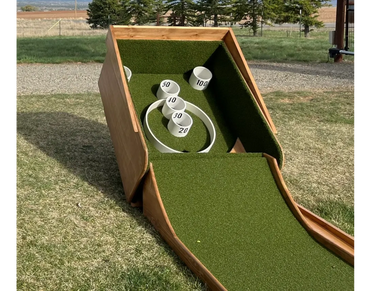 A wooden skee-ball game set outdoors on grass.