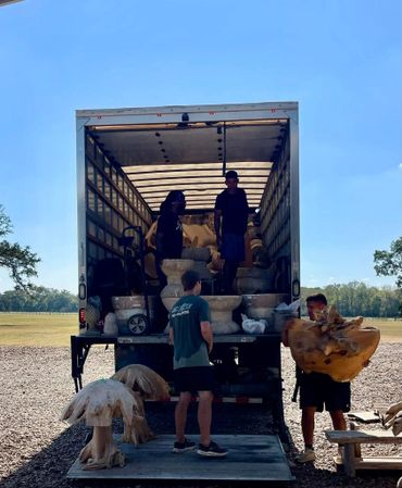 Four men unloading large wooden sculptures from a truck in a sunny open area.