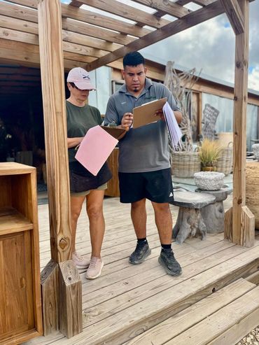 Two people reviewing documents on clipboards under a wooden pergola.