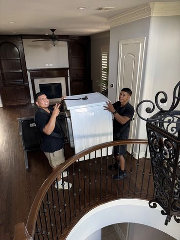 Two men carrying a washing machine up a staircase inside a house.