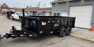Black dual-axle dump trailer parked near garage and houses.