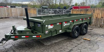 Green Delco dump trailer parked on cracked pavement in a fenced yard.