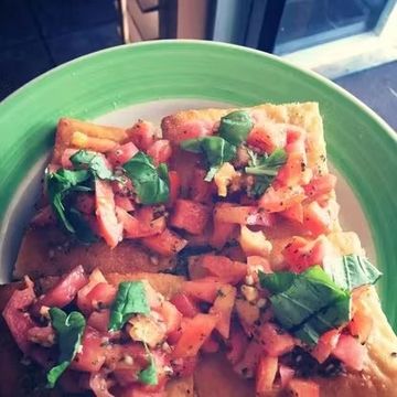 Fresh bruschetta topped with tomatoes and basil on a green plate.