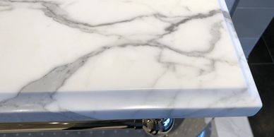 Close-up of a white marble countertop corner with gray veins and polished metal fixtures.