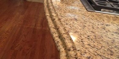 Close-up of a polished granite kitchen countertop with a stove and red kettle.