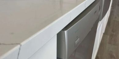 Close-up of a white marble countertop with subtle grey veins above a stainless steel dishwasher.