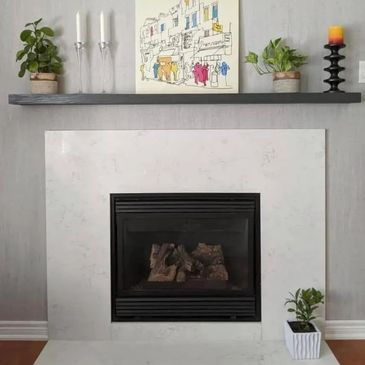 Minimalist fireplace setup with plants, candles, and artwork on a floating shelf.