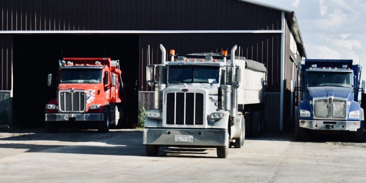 Three large trucks parked outside a warehouse or garage building.