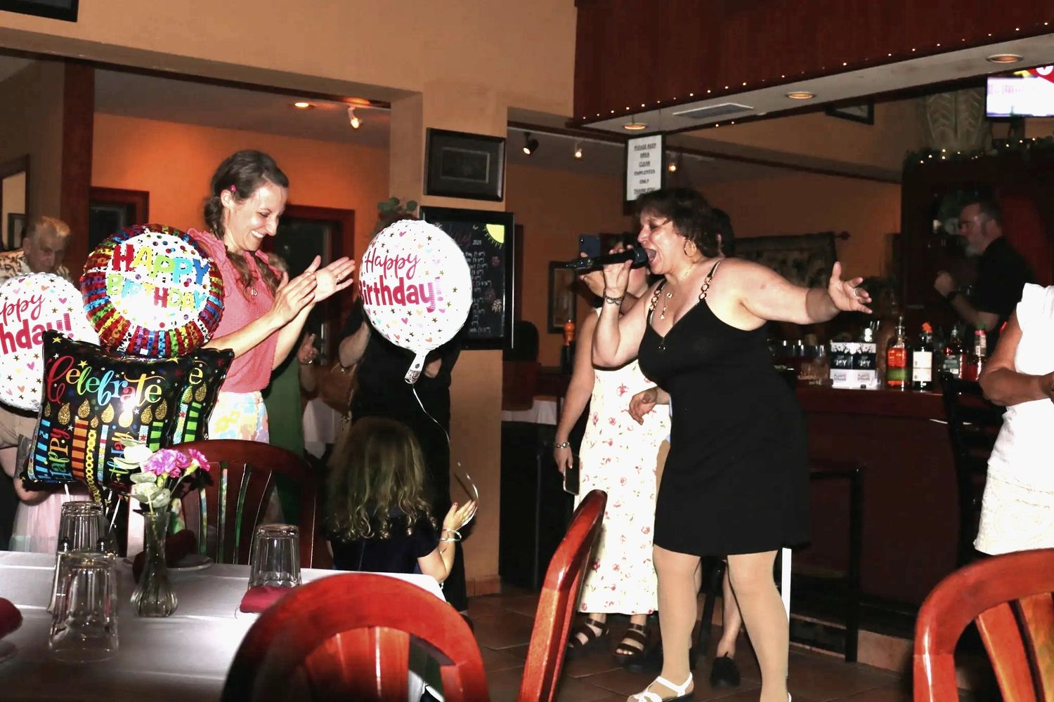 Woman singing at a lively birthday party with guests clapping and celebrating.