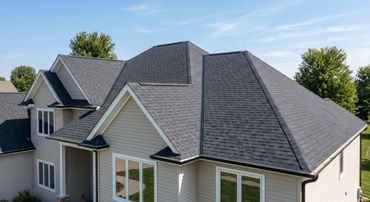 Modern house with a dark shingled roof and beige siding under a clear blue sky.