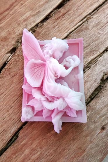 Pink fairy sculpture with delicate wings on rustic wooden surface.