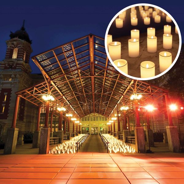 A night time photo showing the entrance to Ellis Island building lined with candles.
