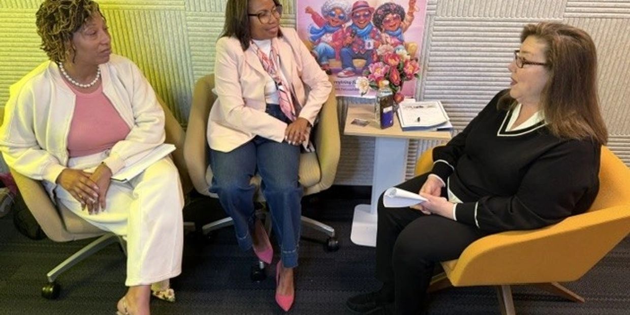 Three women engaged in a conversation while seated in an office setting.