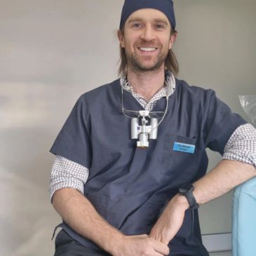 Smiling male dentist in scrubs with dental loupes around his neck.