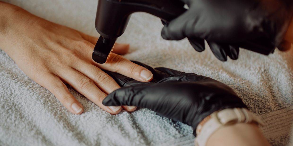Close-up of a hand receiving nail treatment with a tool by a gloved technician.