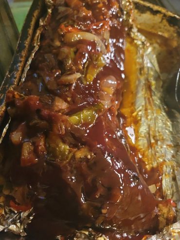 Barbecue ribs covered in sauce with vegetables on foil.