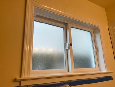 A frosted glass window with white trim and painter's tape at the bottom.
