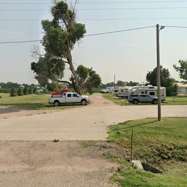 Rural area with pickup trucks, RVs, and green fields under a clear sky.