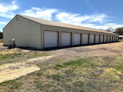 Long beige storage building with multiple closed garage doors under a blue sky.