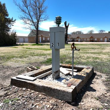 Utility hookup with numbered boxes and a water faucet in a grassy area near buildings.