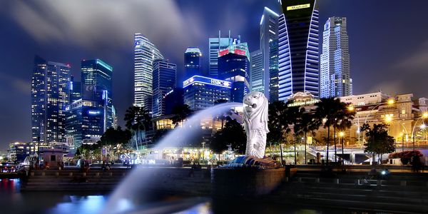 Night view of the Singapore skyline with the iconic Merlion fountain in the foreground.