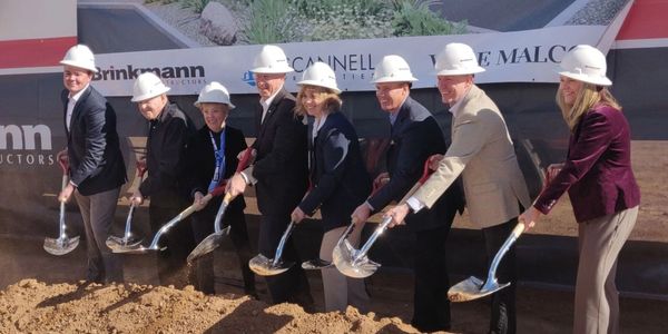 group of eight individuals in hard hats shoveling dirt at groundbreaking ceremony