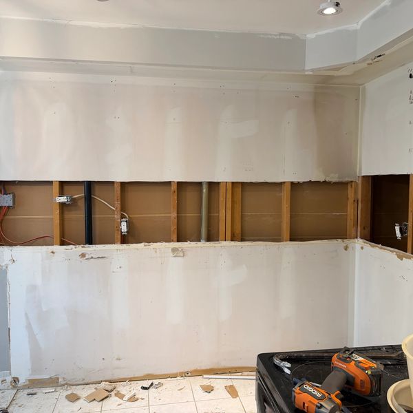 Wall partially stripped down to studs with tools on the floor.