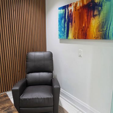 A cozy corner with a leather chair and colorful abstract painting.