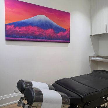 Chiropractic treatment room with black leather table and vibrant mountain painting.